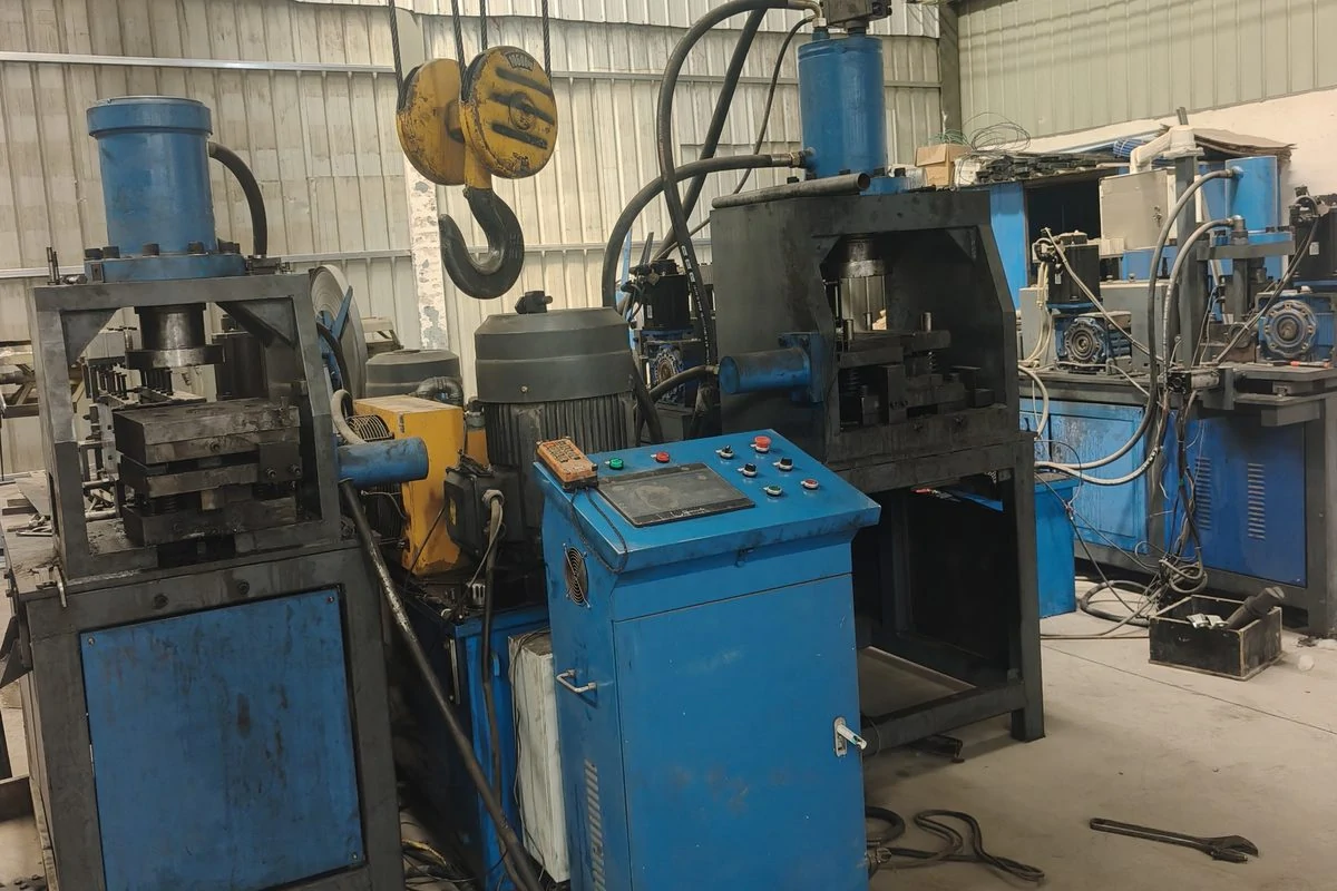 Three blue hydraulic punching machines with hoses and a control cabinet in the workshop