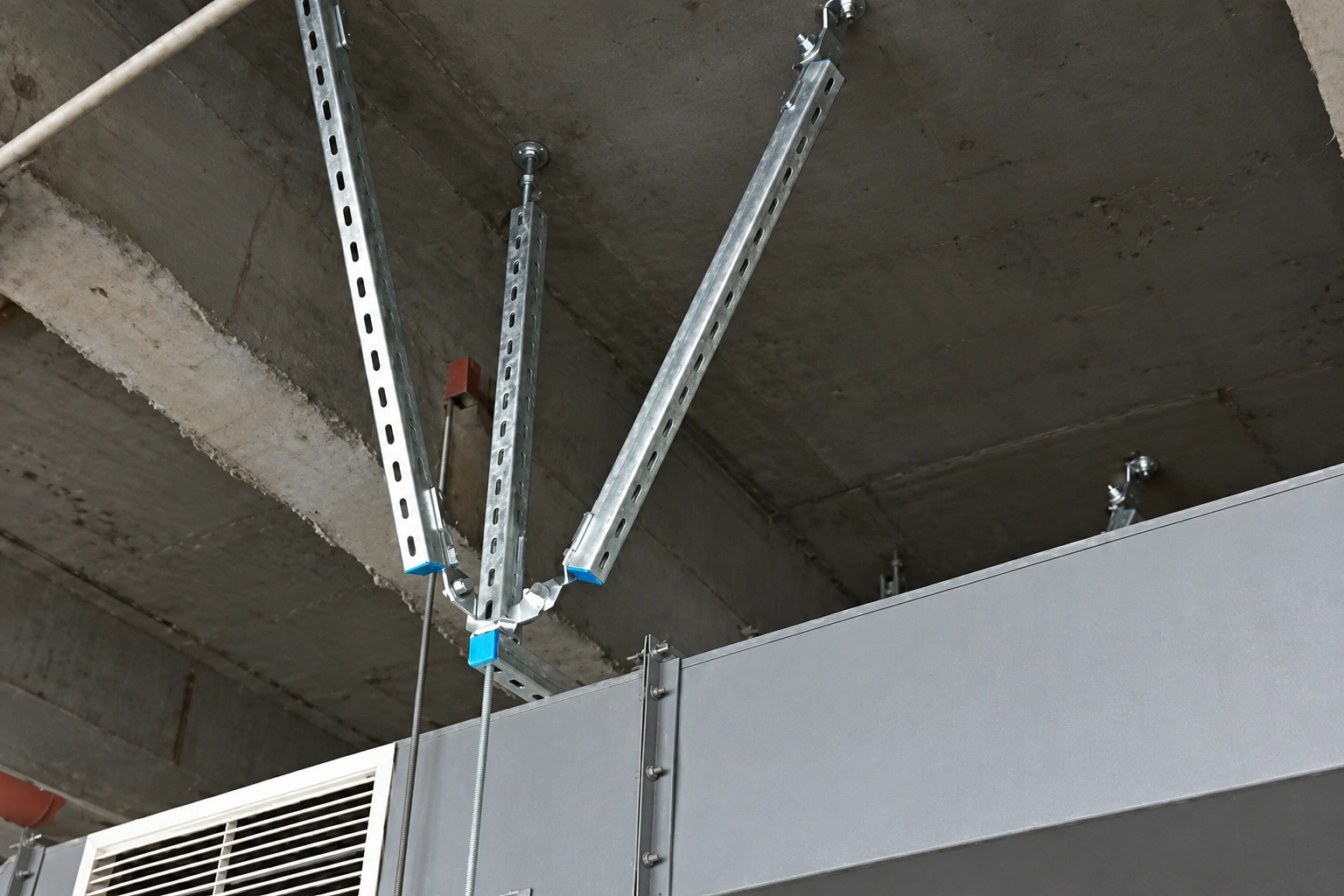 Three slotted stainless steel strut braces bolted to a fixed base fitting below a concrete soffit