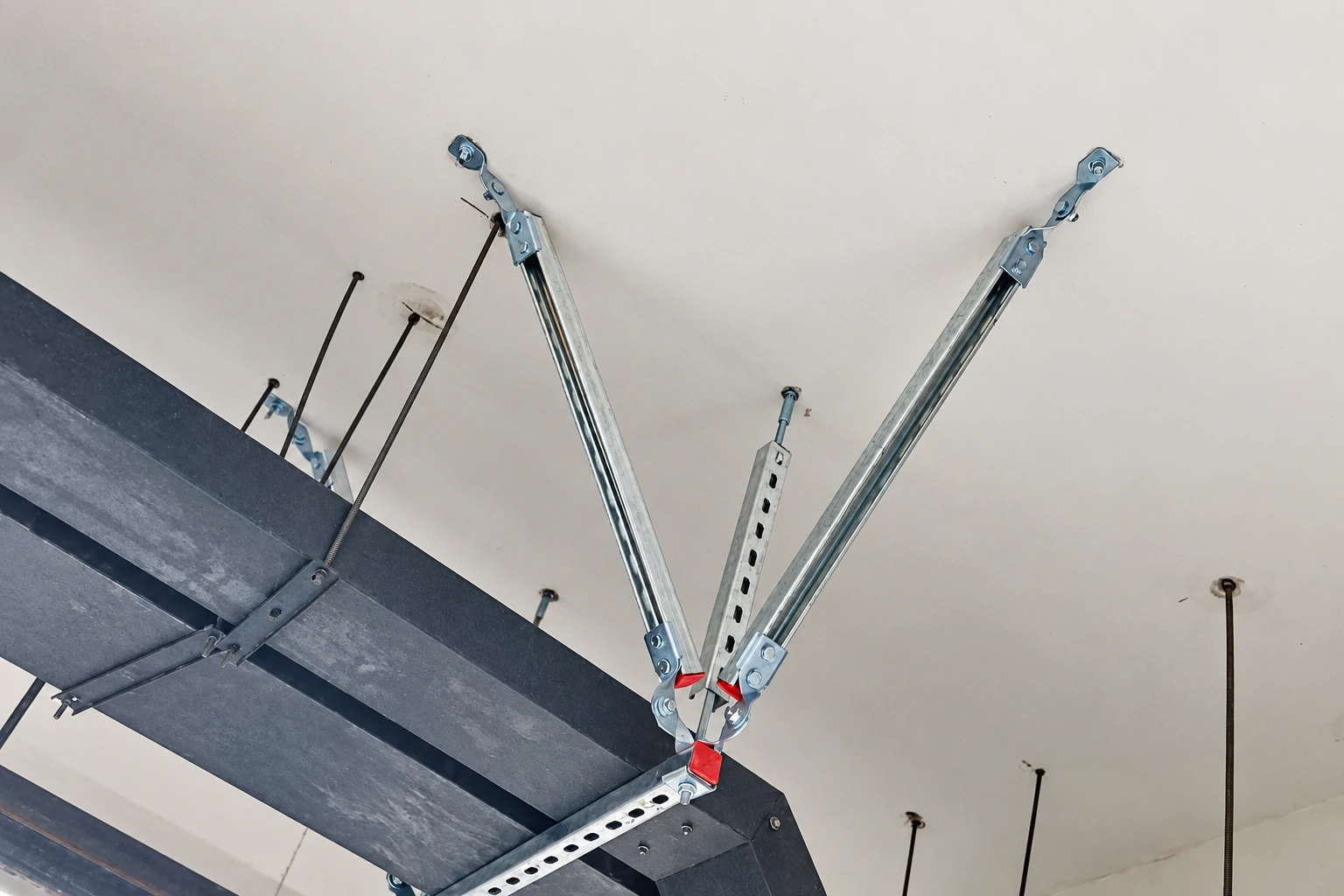 Seismic brace assembly with two diagonal struts and a vertical slotted strut attached below a ceiling
