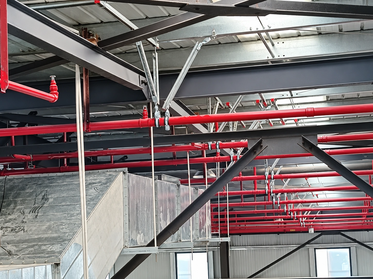 Industrial hall with a red sprinkler network, ductwork and suspended channel supports