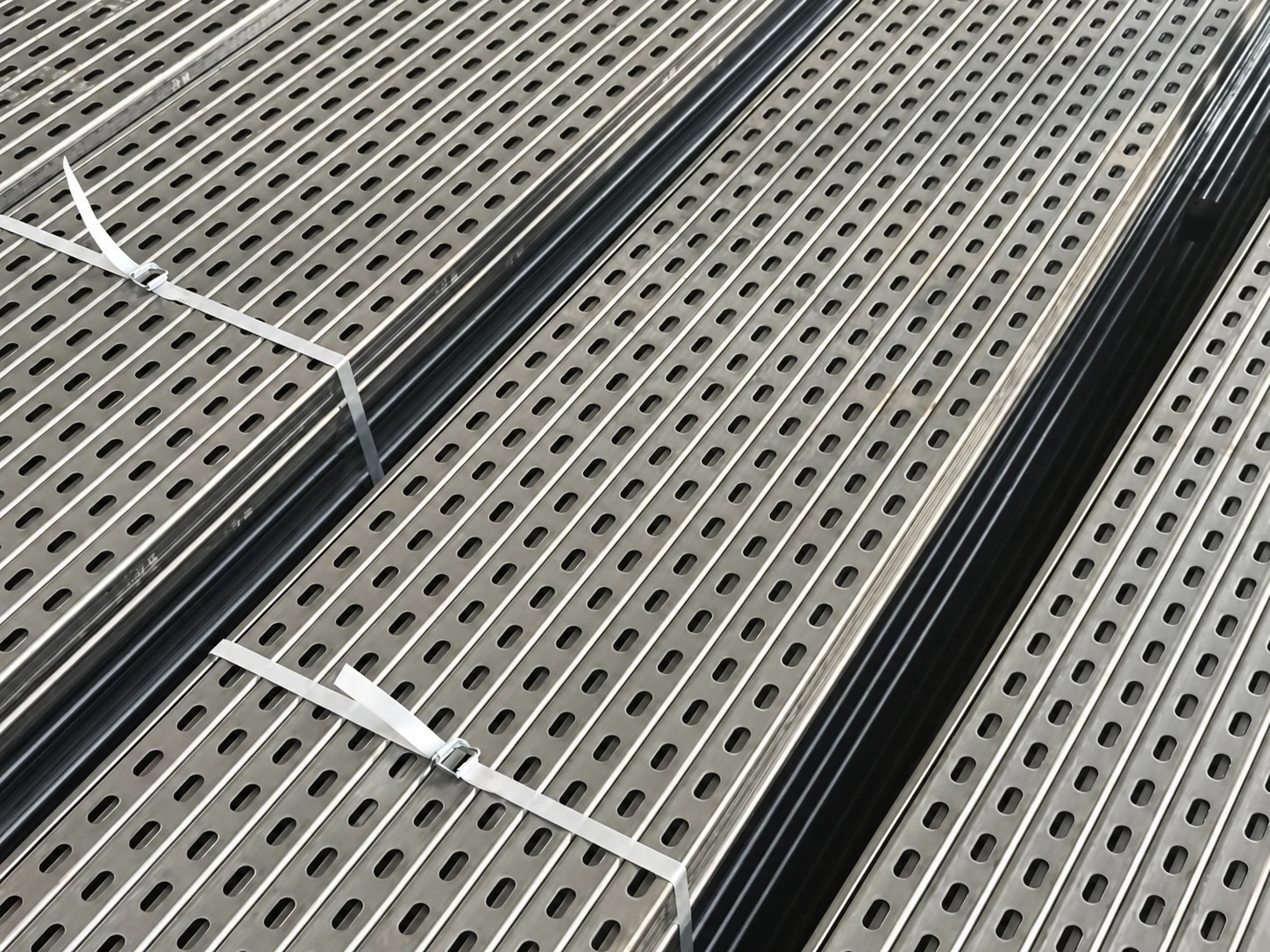 Strapped bundles of galvanised slotted strut channel with continuous perforations stacked in the workshop