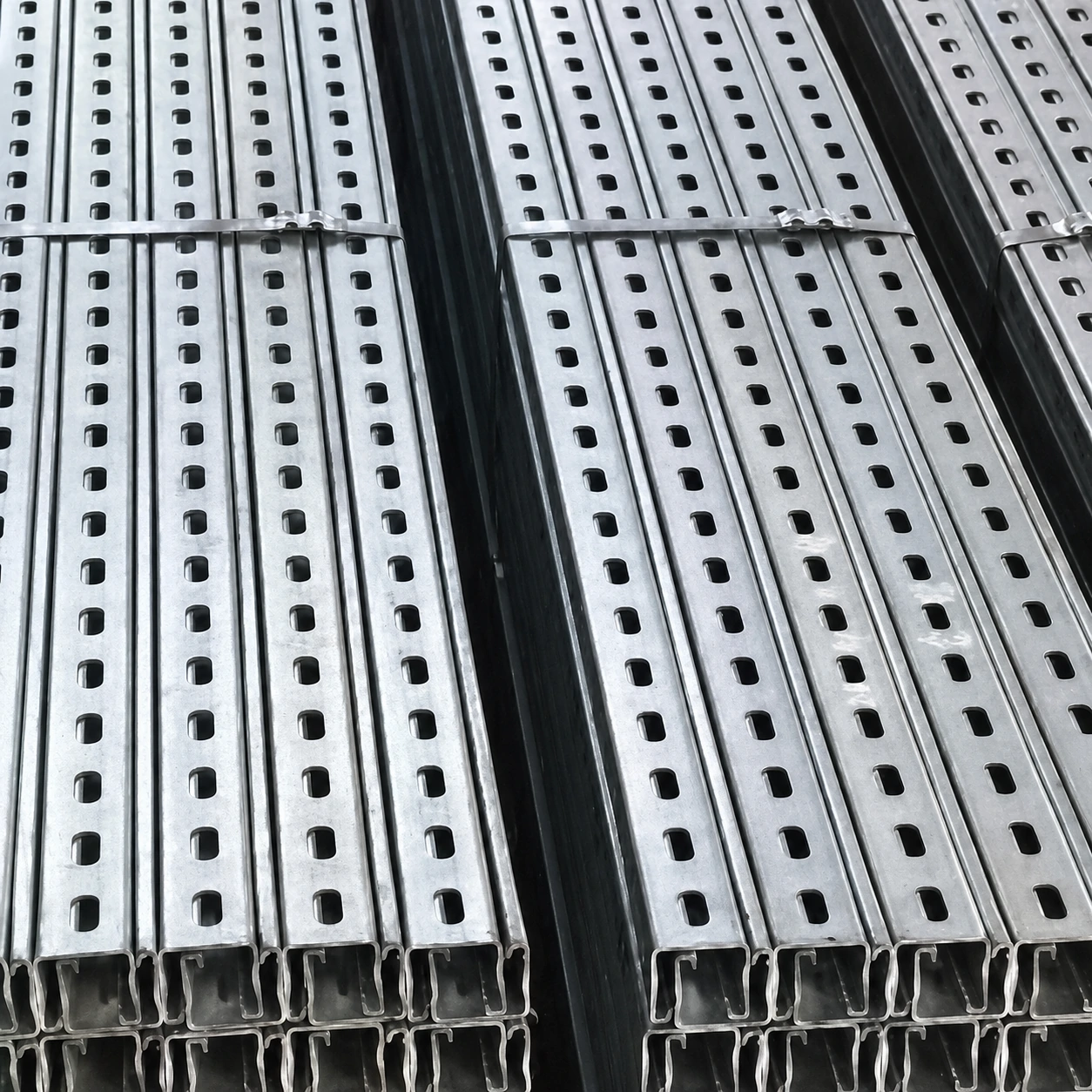 Bundles of galvanised slotted strut channel stacked with their open C-shaped ends facing the camera