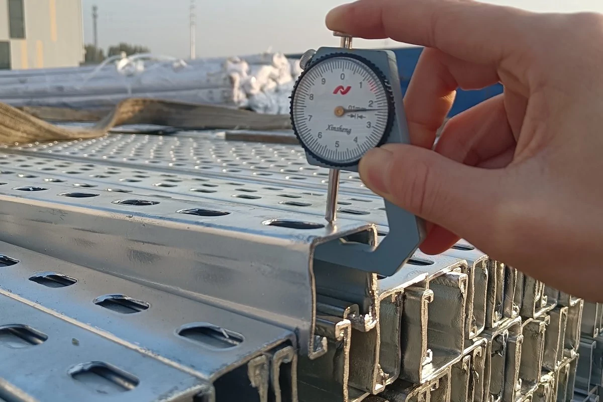 Dial gauge held against the edge of a galvanised strut channel in the factory yard