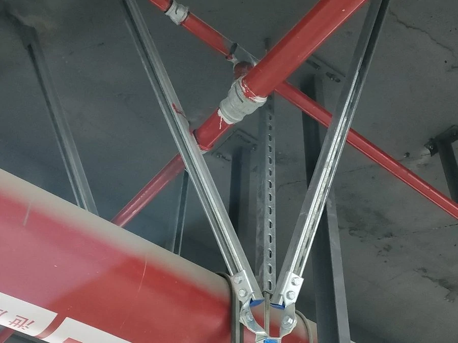 V-shaped seismic brace of galvanised slotted channel bolted to blue clamp brackets on a red fire pipe