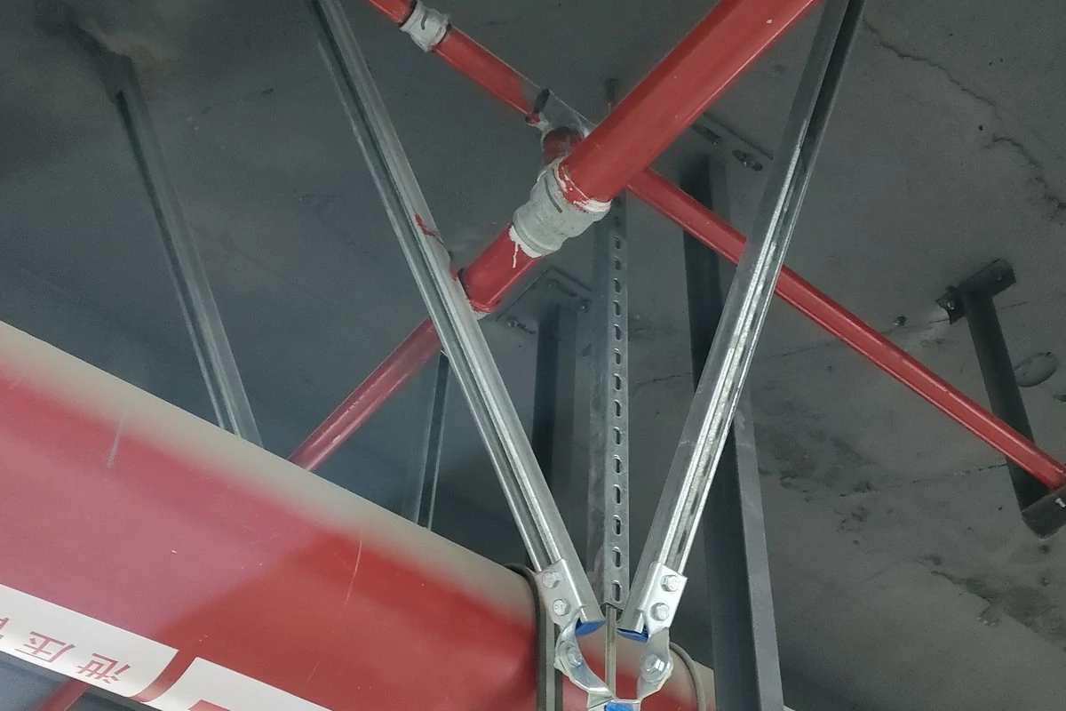 V-shaped seismic brace of galvanised slotted channel bolted to blue clamp brackets on a red fire pipe