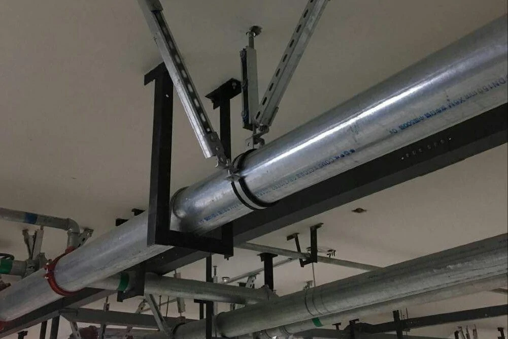 Large galvanised pipe on a black steel trapeze hanger braced by two diagonal slotted struts